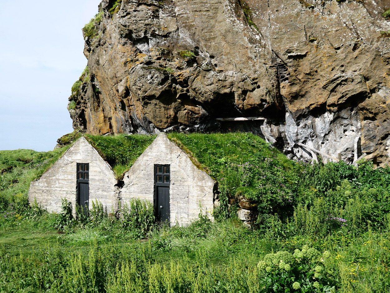 Zwei kleine isländische Hütten unter einem Felsen